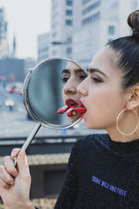 Woman carrying toy car in mouth by mirror in city