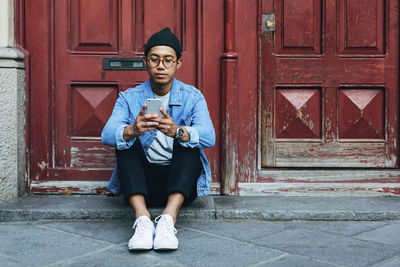 Man using smart phone while sitting on doorway