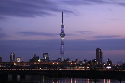 Communications tower in city against cloudy sky