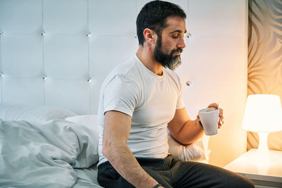 Person with some kind of problem sitting on the bed with a cup and looking lost