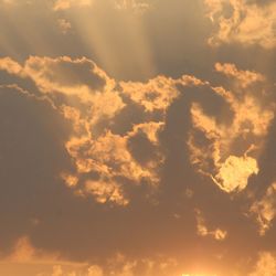 Low angle view of sunlight streaming through clouds