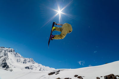 Snowboarder jumps from a big air with a board grab, a nose or tail trick in rotation, against the