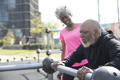 Man exercising while leaning on railing by woman at park
