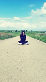 Full length of woman sitting on road against sky