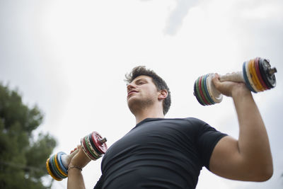 Low angle view of young man looking at camera against sky