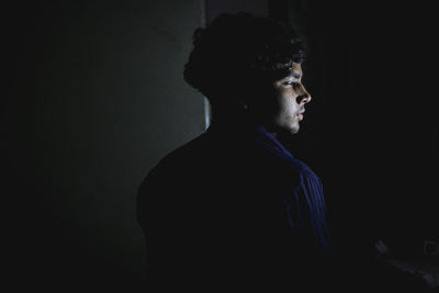 Side view of young man looking away against black background