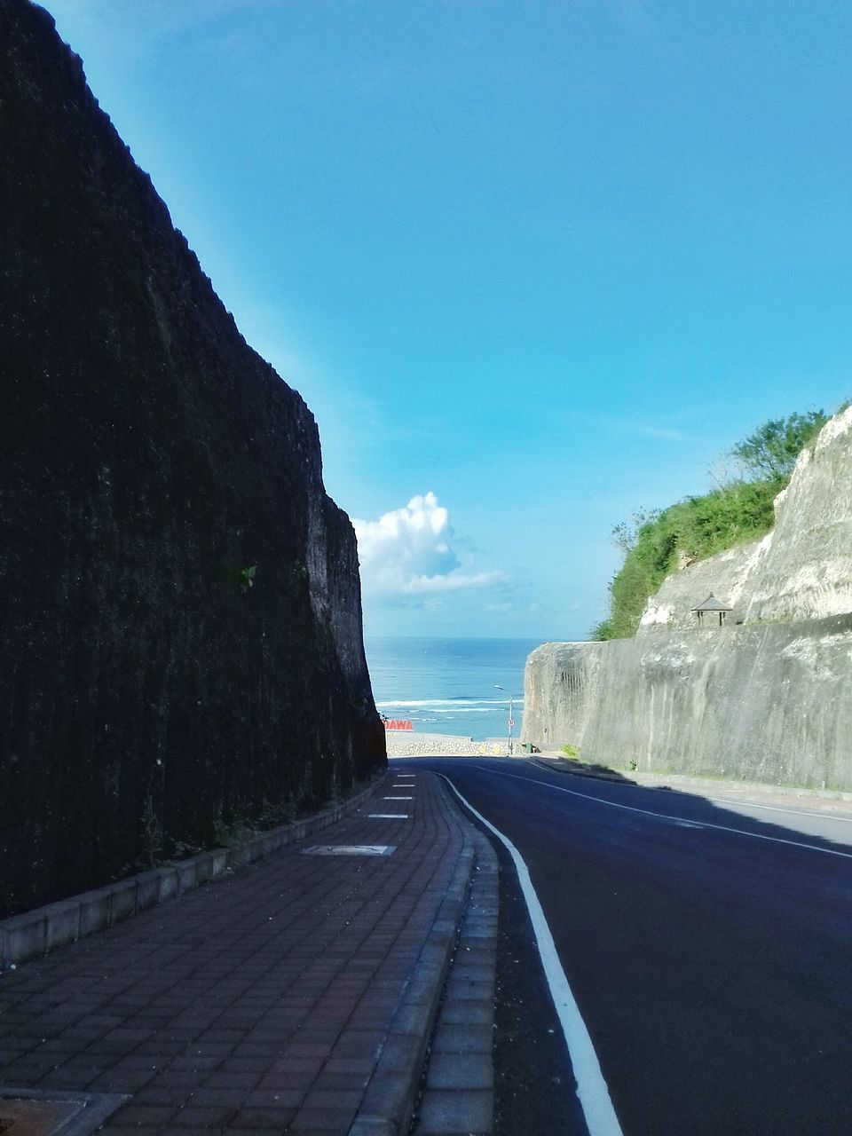 ROAD AMIDST SEA AGAINST BLUE SKY