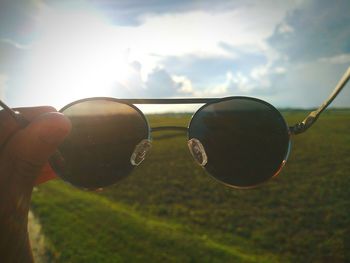 Close-up of hand holding sunglasses against sky