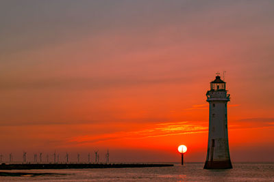 Lighthouse by sea against orange sky