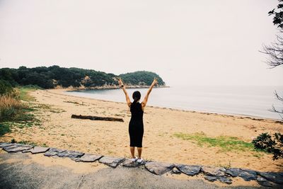 Rear view of woman standing on beach against clear sky