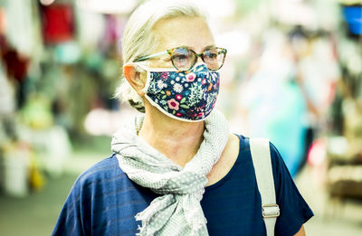 Close-up of senior woman wearing mask looking away while standing outdoors