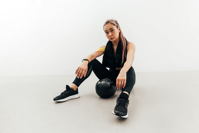 Portrait of young woman sitting on floor against white background