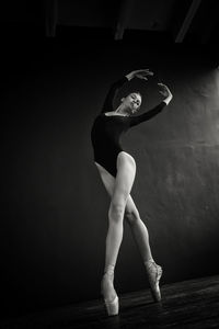 A ballerina in a bodysuit and pointe shoes moves around the room with long strides