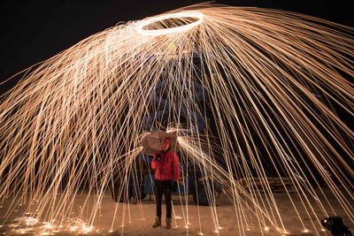 Young man with umbrella standing below wire wool at night