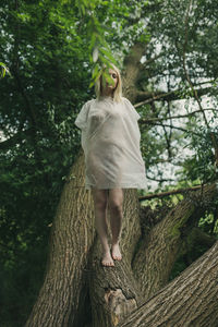 Woman standing by tree trunk in forest