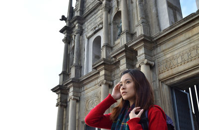 Young woman looking away against building