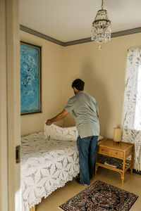Full length of young male nurse making bed at home