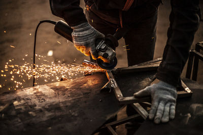 Midsection of worker grinding metal in factory