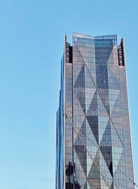 Low angle view of glass building against clear blue sky