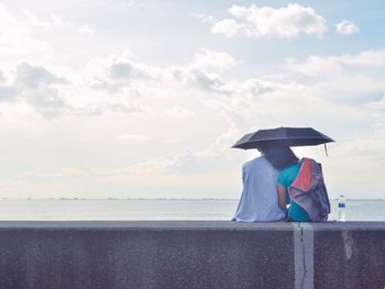 Man sitting on beach against sky