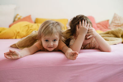 Kids playing on colorful bed in the morning hide-and-seek. happy child lie on pink bed. sister and