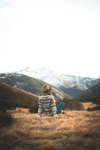 Rear view of woman sitting on field against sky