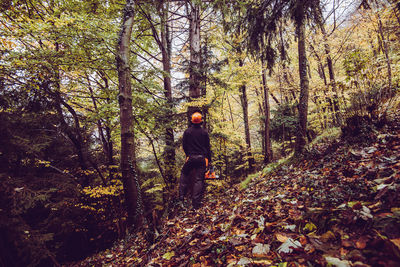 Full length of woodcutter man with chainsaw in forest