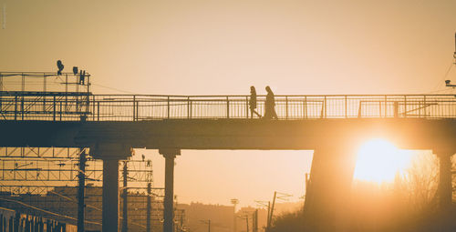 Low angle view of silhouette people walking on bridge during sunset
