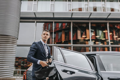 Businessman disembarking from car in front of building