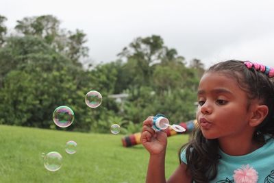 Close-up of girl blowing bubbles on field