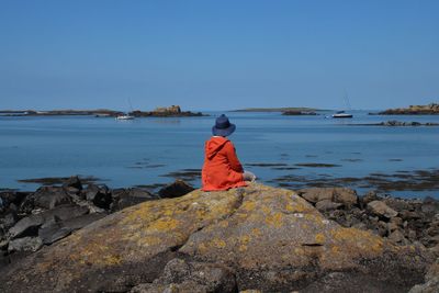 Rear view of person sitting on rock against sea