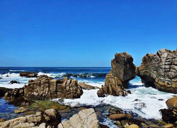 Rocks on sea shore against clear blue sky