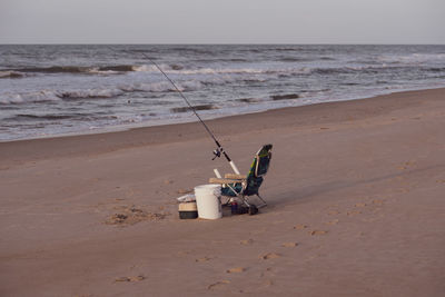 Fishing rod on sand at beach against sky
