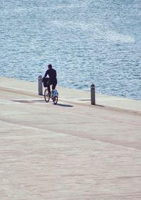 Rear view of man riding bicycle by sea