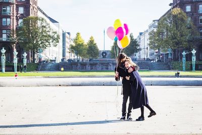 Full length of happy couple with balloons in city