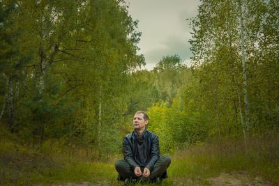 Young man sitting on land against trees in forest