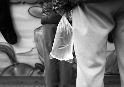 Midsection of man holding fish in plastic bag while standing outdoors