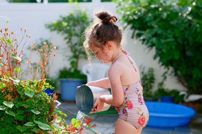 Cute young girl watering plants with a bucket on a summer day in the backyard