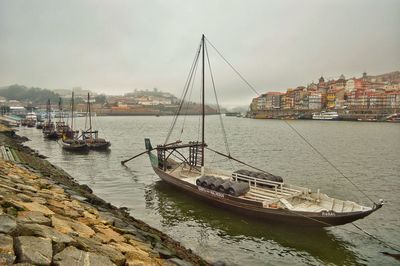 Boats sailing on river by city against sky