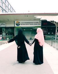 Women in burka holding hands against building