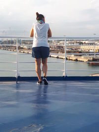 Full length rear view of woman standing on railing against sea