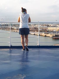 Rear view of mid adult woman looking at cityscape while standing by railing against sky