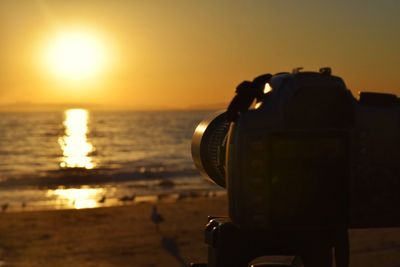 Close-up of camera at beach against sky during sunset