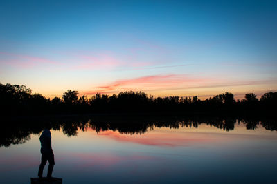 Silhouette person by lake against sky during sunset