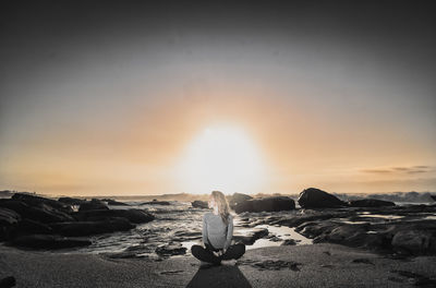 Woman sitting at beach against clear sky during sunset