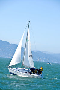 People sailing on sailboat in sea against sky