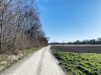 Empty road amidst field against sky