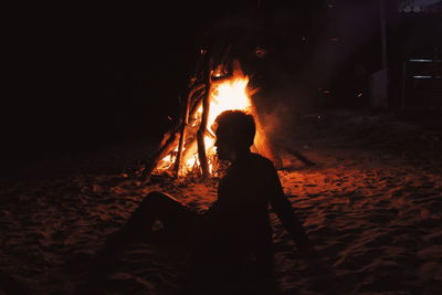 Silhouette woman standing by illuminated bonfire against sky at night