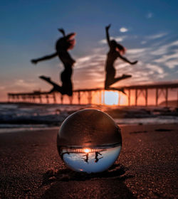 Upside down image of silhouette ball on beach against sky during sunset