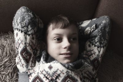 Boy in christmas sweater lying contented on sofa and smiling with positive emotion on his face